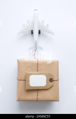 Flat lay of wrapped package with blank tag and airplane model on white background. Shipping logistics transport minimal creative concept. Stock Photo