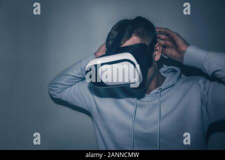A young man looks into virtual reality glasses close-up on the blue background. Stock Photo