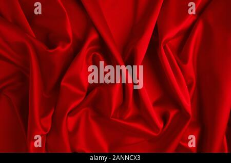 Red silk fabric lying in form of waves, close-up. Stock Photo