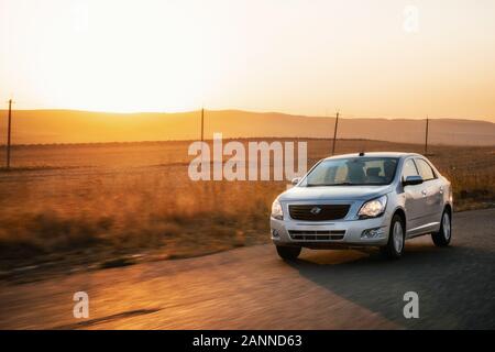 Silver sedan Ravon r4 Cobalt car driving fast on countryside asphalt road at sunset, Uzbekistan Stock Photo