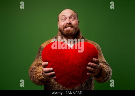 Man holds red toy heart while standing on empty green background in studio Stock Photo