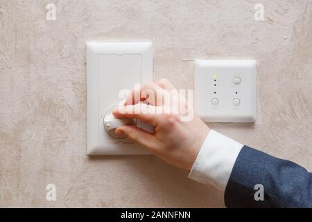 Man regulating temperature on air conditioning controller thermostat on the wall Stock Photo