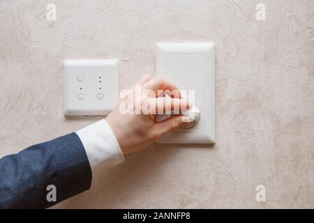 Man regulating temperature on air conditioning controller thermostat on the wall Stock Photo