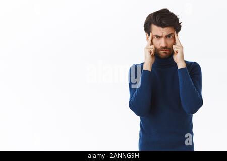 Guy trying think straight, focus on task, standing in high neck sweater, touching temples and purse lips, frowning and look camera concentrated, tryin Stock Photo