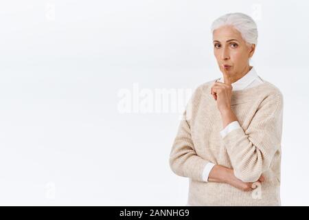 Strict and elegant serious-looking smart senior lady, teacher or principal, grandmother tutoring child, shushing at camera, keep quiet, make hush gest Stock Photo