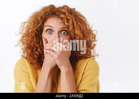 Close-up shocked or scared, speechless attractive redhead curly woman in yellow sweater, gasping shook, stare camera with popped eyes, witness disaste Stock Photo