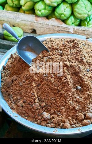 A bowl with unrefined brown sugar, called Muscovado, next to green sayute vegetables for sale at a street market in Capiz Province, Philippines Stock Photo
