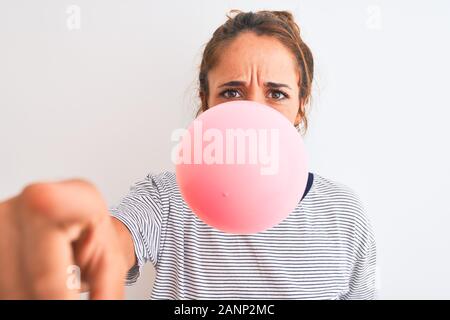 Young redhead woman chewing gum and blowing hair bubble over white isolated background pointing with finger to the camera and to you, hand sign, posit Stock Photo