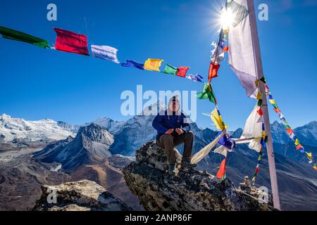 Asian hiker sitting on the cliff in Nangkartsang Peak, Everest Base Camp, with clear blue sky and himalayan mountain range at the background.