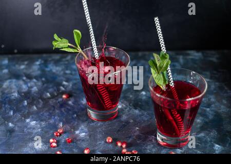Pomegranate juice in transparent glasses. Spray from a falling piece of ice. On a blue background under a stone. Trend 2020. Grains are scattered near Stock Photo