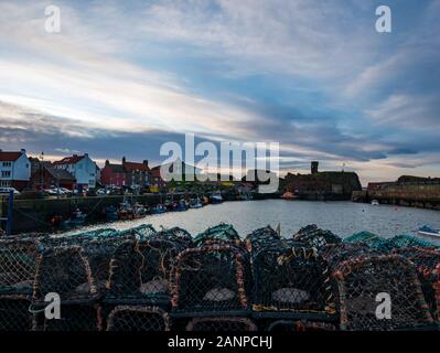 Dunbar, East Lothian, Scotland, United Kingdom, 18th January 2020. UK Weather: Sunset view over Dunbar Harbour with fishing boats and the outline of ruins of Dunbar Castle with lobster pots or creels on the harbourside Stock Photo