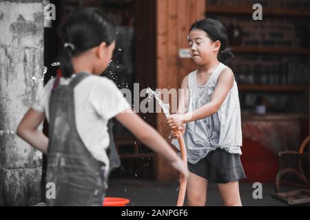 Pingan, China -  August 2019 : Two little Chinese girls playing with water hose in a small village  in summer Stock Photo