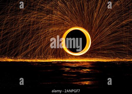 Steel wool painting with light in darkness spark effect and reflections on wet ground Stock Photo