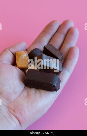 Hand with chocolates on a pink background. Enjoying sweets. Sweet addiction concept. The concept of love for sweets. Vertical photo. Stock Photo