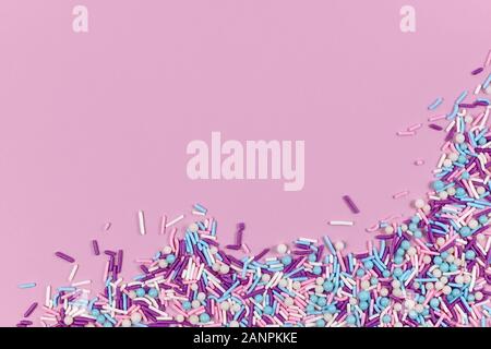 Colorful white, pink, blue and purple sugar sprinkles in shape of balls and sticks on pink background with blank copy space Stock Photo