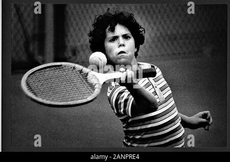8 year old boy learning to play tennis at camp real concentration in southern California face, wooden racket, ball, watching Stock Photo