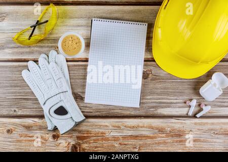 Safety helmets, glasses for workplace office table construction with notebook, cup of coffee wireless charging case headphones protective gloves on wo Stock Photo