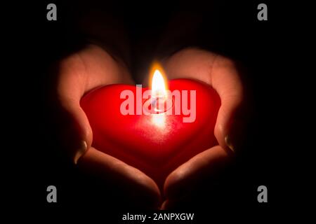 Female hands holding a heart-shaped candle in the dark Stock Photo