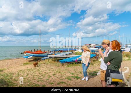 Whitstable England - August 18 2019; People eating ice cream and with dog on leads standing on waterfront where small boats and yachts are on beach. Stock Photo