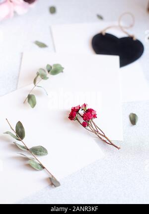 Background with copy space blank on table with black heart, eucalyptus branch, roses flowers and leafs. White paper top view, flat lay, minimal style. Stock Photo