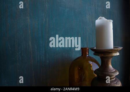 Big brown glass jar with coins and massive candleholder with white candle on it on blue shabby wall background, concept of savings, trading, savings Stock Photo