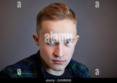 Close-up dramatic portrait of a white blue-eyed male on a dark gray background. The serious face of a young Caucasian man with gray eyes and a short h Stock Photo