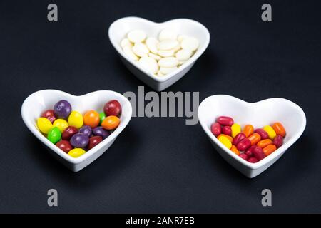 Heart shaped saucer filled with colorful candies on a black background. Valentine's Day illustration. Top views