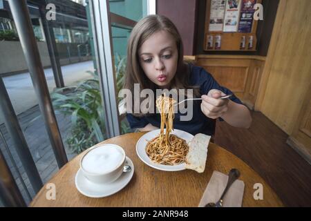 Young caucasian woman girl eating Italian pasta with funny face expression in a cafe, restaurant Stock Photo