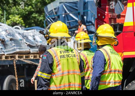 South African firemen, firefighters from the fire and rescue service team overseeing a road accident where a jackknifed truck has lost its load Stock Photo