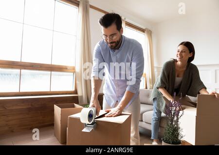 Happy young family packing boxes with tape dispenser Stock Photo