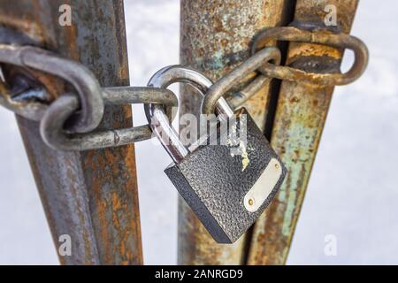 Closed padlock and chains hanging on old and rusty iron gates Stock Photo