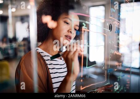 Woman working and writing on the glass board in office. Business, technology, research concept Stock Photo