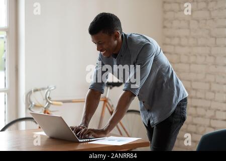 Smiling African American businessman using laptop, standing near desk Stock Photo