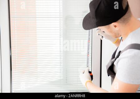 Worker in uniform installing blinds on plastic upvc window Stock Photo