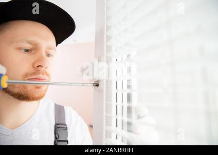 Construction worker man uses screwdriver to screw handle install plastic white upvc windows in house Stock Photo