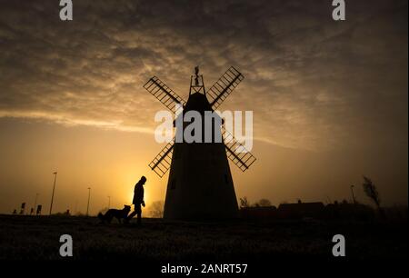 A man takes his dog for a walk as the sun rises behind the Allen Clarke Memorial Windmill in Blackpool, as the chilly weekend continued with the mercury dipping below zero and fog coating large parts of the country. Stock Photo