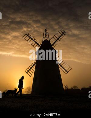 A man takes his dog for a walk as the sun rises behind the Allen Clarke Memorial Windmill in Blackpool, as the chilly weekend continued with the mercury dipping below zero and fog coating large parts of the country. Stock Photo