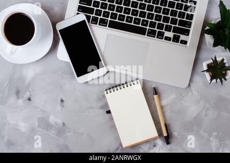 White smartphone with black blank screen on office desk with laptop and cup of coffee on gray concrete. Mock up of phone. Business or education concep Stock Photo