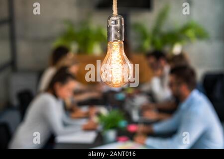Young business people are discussing together a new startup project. A glowing light bulb as a new idea. Stock Photo