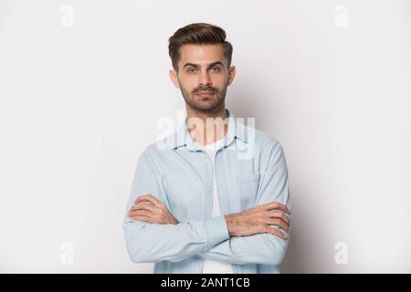 Portrait of serious confident millennial guy with folded hands. Stock Photo