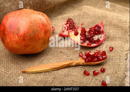 Ripe juicy pomegranate, pieces of pomegranate and pomegranate seeds on a wooden spoon on a background of rough homespun fabric. Close up Stock Photo