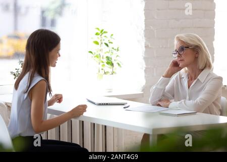 Sceptic aged HR manager listens young vacancy applicant during interview Stock Photo