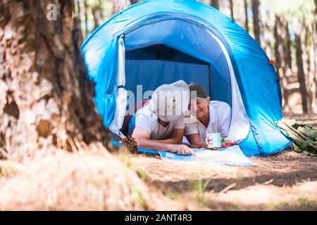 Alternative travel vacation in the forest for senior old happy cheerful caucasian couple together inside a tent lookoing a map and choosing the next d Stock Photo