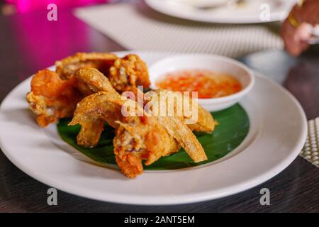 Thai style deep fried crispy chicken wing, serve on white dish with spicy sweet sauce on side. Thai famous appetizer dish. Stock Photo
