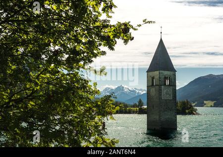 Bell tower of a church sunken in Lake Reschen with snow covered alps in the distance, Reschensee/Lago di Resia, South-Tirol, Italy Stock Photo