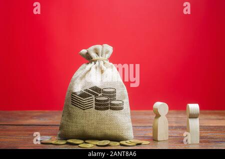 Money bag and two wooden figures of people. Business and finance concept. Businessmen are discussing the company's profit. Search for sources of fundi Stock Photo