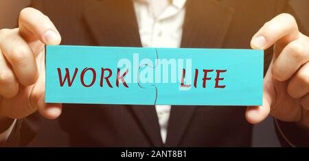 A man collects wooden puzzles with the words Work and Life. The concept of paying attention to the life values, promotion at work. Right balance. Harm Stock Photo