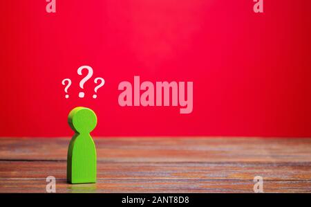 A miniature green man and question marks above him. Uncertainty. Search for an answer to a question. Problems and solutions concept. Riddle mystery, i Stock Photo
