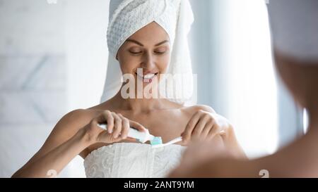 Beautiful woman wearing towel on head applying toothpaste on toothbrush Stock Photo