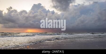 Panorama of a sunset and storm clouds over sea. Scenic view at the beach when the setting sun is between the horizon and the rough sea. Stock Photo